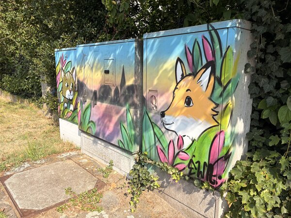 Drei Stromkästen, die mit Grafitti bemalt wurden und in der Mitte die Skyline von Schüttorf zeigen. Rechts ist ein Fuchs und links eine Katze abgebildet.