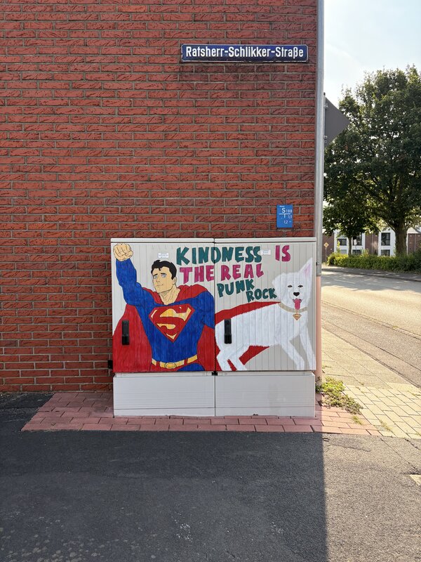Ein Stromkasten, der mit Grafitti bemalt wurde und Superman mit einem weißen Hund abbildet.