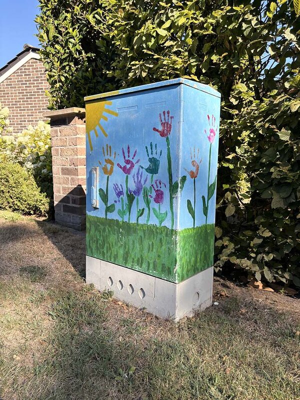 Ein Stromkasten, der mit Grafitti bemalt wurde und wo eine Sonne und Blumen mit Händen als Blüten zu sehen sind