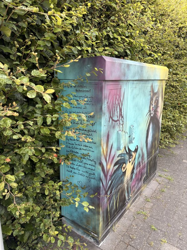 Ein Stromkasten, der mit Grafitti bemalt wurde und eine Katze und einen Igel abbildet.