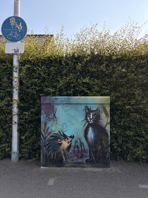 Ein Stromkasten, der mit Grafitti bemalt wurde und eine Katze und einen Igel abbildet.