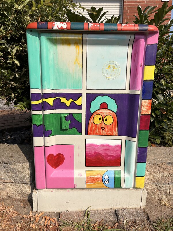 Ein Stromkasten, der mit Grafitti bemalt wurde mit mehreren bunten Motiven und Farben