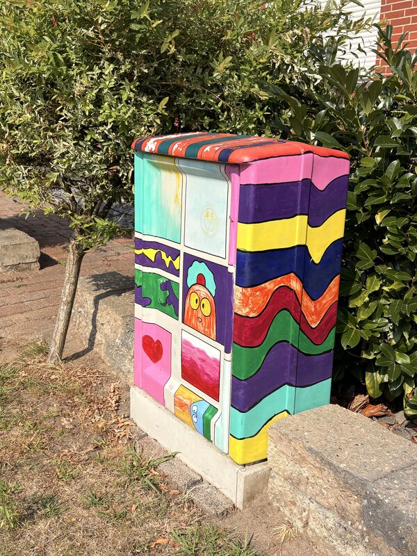 Ein Stromkasten, der mit Grafitti bemalt wurde mit mehreren bunten Motiven und Farben