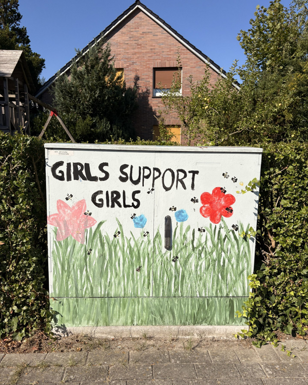 Ein Stromkasten, der mit Grafitti bemalt wurde und Gras, Blumen und Bienen mit der Aufschrift "Girls support Girls", abbildet