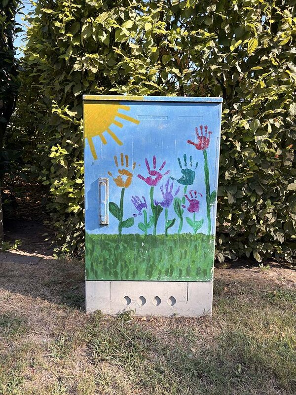 Ein Stromkasten, der mit Grafitti bemalt wurde und wo eine Sonne und Blumen mit Händen als Blüten zu sehen sind