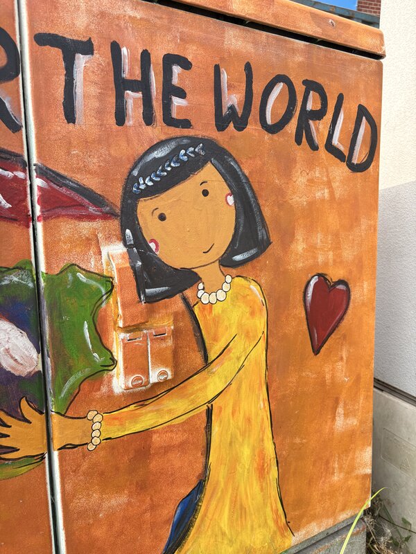 Ein Stromkasten, der mit Grafitti bemalt wurde und der eine Frau abbildet, die die Welt umarmt mit dem Schriftzug "Pray for the World"