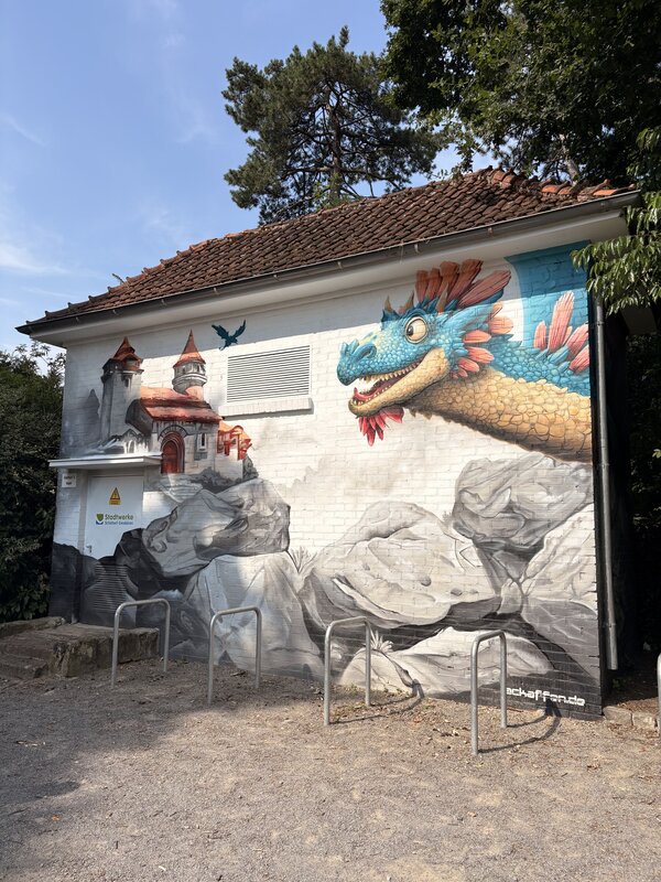 Eine großes Trafohaus, das mit Grafitti bemalt wurde und eine Burg und einen Drachen abbildet.