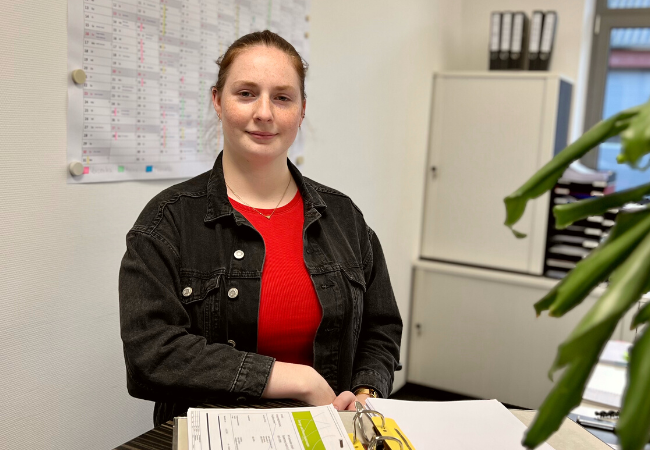 Mädchen mit rotem T-shirt und schwarzer Jacke sitzt am Schreibtisch