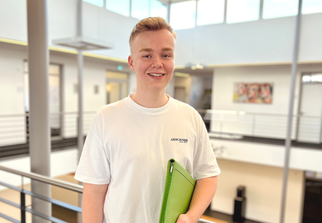 Junge mit weißem T-shirt hält eine grüne Mappe in der Hand