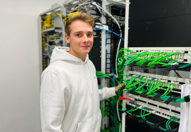 Junge mit weißem Pullover steht vor einem Elektroschrank