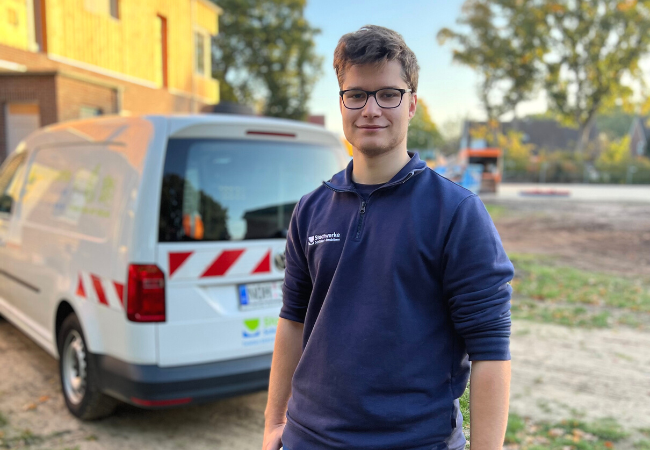 Junge mit blauem Pullover steht vor einem weißen Auto