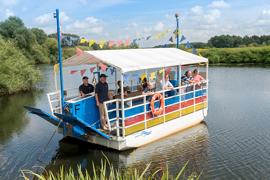 Mehrere Personen fahren auf einer Fähre über einen Fluss