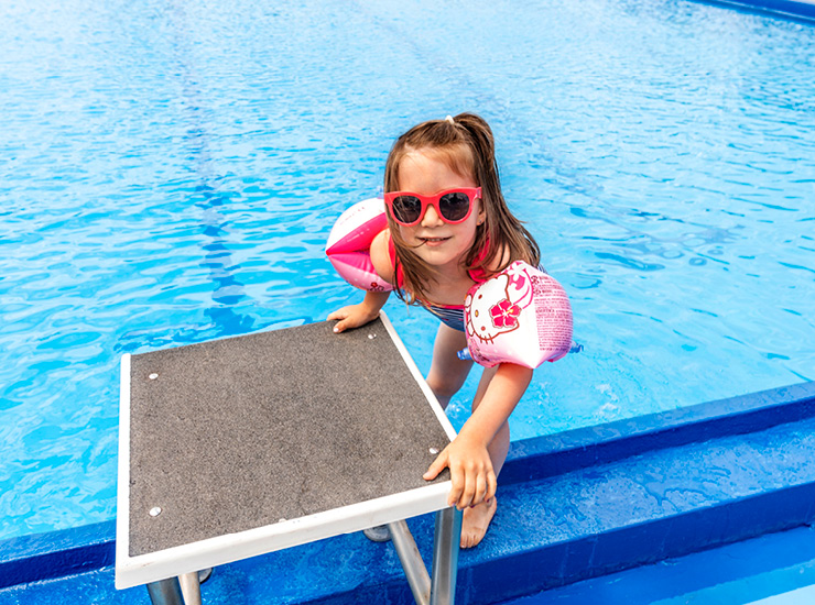 Kind mit Schwimmflügeln steht am Rand eines Schwimmbeckens