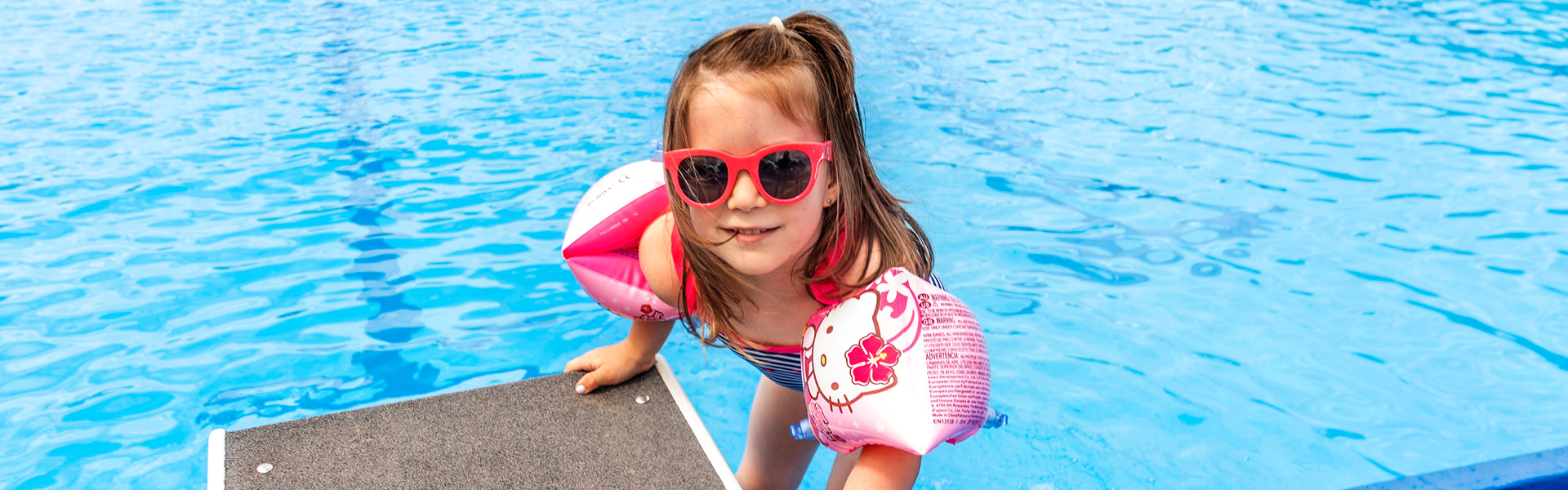 Kind mit Schwimmflügeln steht am Rand eines Schwimmbeckens