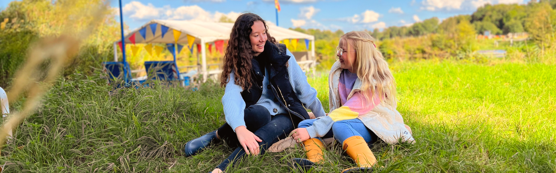 Zwei Mädchen sitzen auf einer Wiese und lächeln sich an