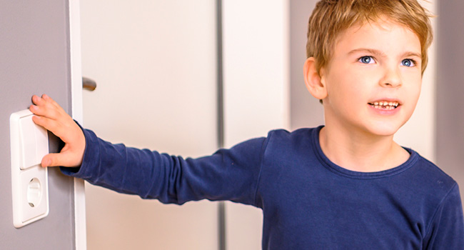 Ein kleiner Junge im blauen Pullover drückt auf einen Lichtschalter